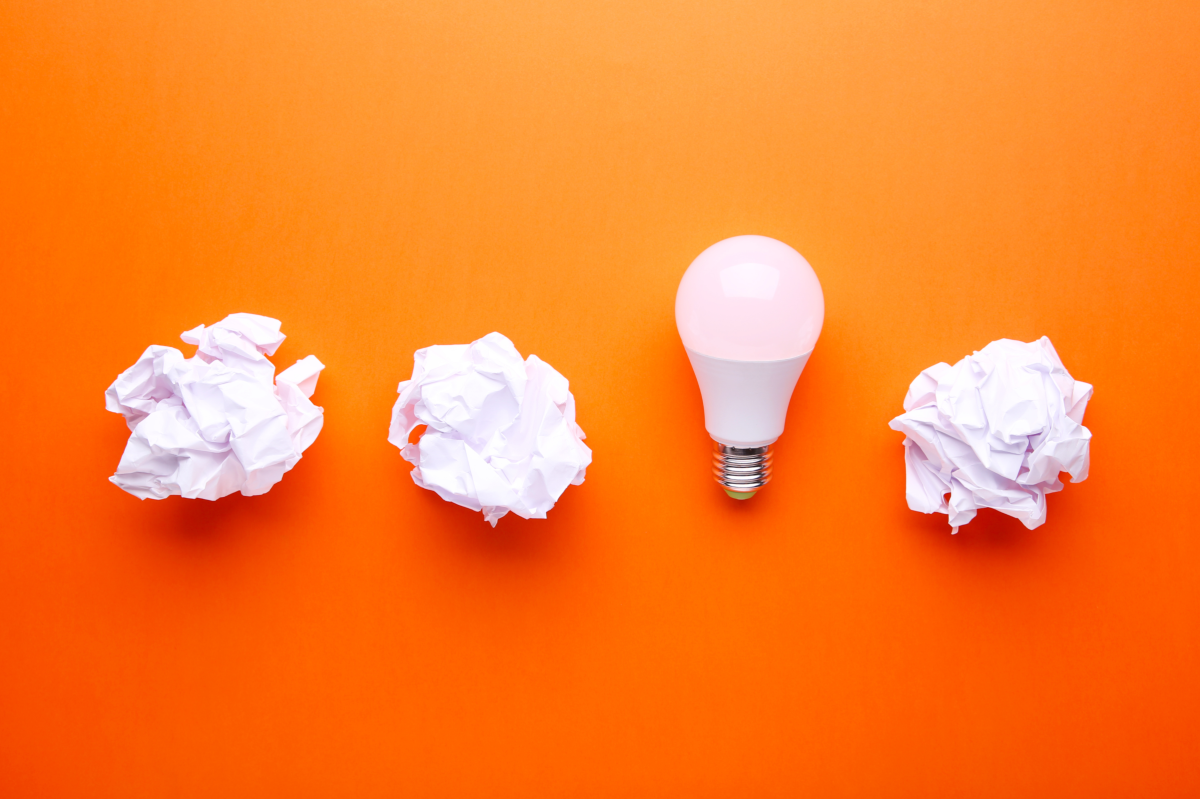 Een gloeilamp, omringd door drie verfrommelde stukken wit papier